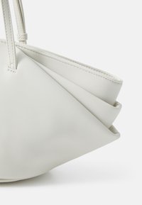 Sac à main en cuir blanc avec un design unique replié, des bords surpiqués et des anses allongées. Texture lisse avec une finition mate.