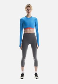 Blue long-sleeve crop top with red accent, paired with high-waisted gray leggings. Features smooth texture and snug fit. Black athletic shoes.