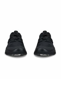 Musta urheilukenkä, jossa mustavalkoiset kuvioidut nauhat, nähtynä edestä valkoista taustaa vasten.