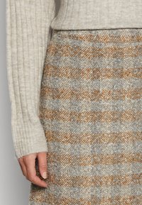 Hame beige, oranssi ja harmaa sävyissä, jossa on houndstooth-kuvio. Teksturoitu kangas, jossa on istuva vyötärö ja sivusaumapussit.