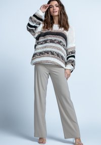 Sweter w paski w kolorze kremowym, brązowym i czarnym, o luźnym kroju. W połączeniu z beżowymi spodniami szerokimi i przejrzystymi obcasami. Tło jest jasnoszare.