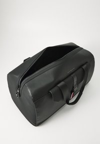 Black duffel bag made from smooth material, featuring a zip closure, dual handles, and a front strap. Compact rectangular shape.