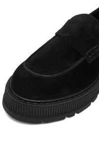 Čierne semišové loafers s okrúhlou špičkou, šitým detailom a textúrovanou gumovou podrážkou so zvislými ryhami.