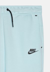 Šviesiai mėlynos sportinės kelnės, pagamintos iš minkštos medžiagos; turi elastingą juosmenį su juodu raišteliu ir juodą Nike logotipą šone.