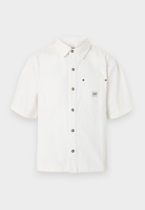 Chemise blanche à manches courtes avec col, boutons métalliques sur le devant, une poche poitrine avec une petite étiquette de la marque Lee.