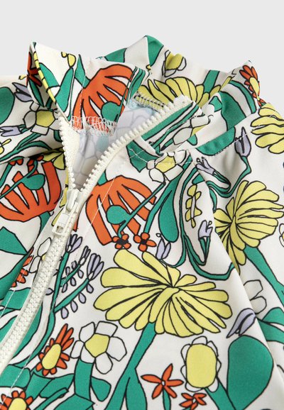Gros plan sur un tissu à imprimé floral coloré avec une fermeture éclair blanche partiellement ouverte sur un vêtement.