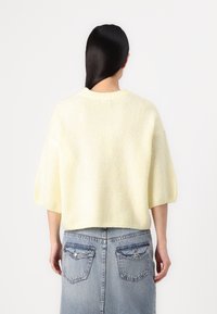 Helles gelbes, kurz geschnittenes Sweatshirt mit kurzen Ärmeln und geripptem Rundhalsausschnitt, kombiniert mit einem Jeansrock mit Gesäßtaschen und geradem Schnitt.