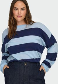Striped sweater featuring light blue and navy blue horizontal stripes, round neckline, soft fabric, and relaxed fit paired with dark denim pants.