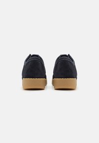 Marina mockasiner i mocka med rundad form, med en sula av gummiklädsel och slät textur. Klacken är synlig, designen är minimalistisk.