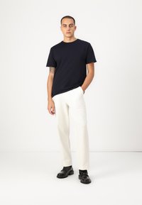 Navy short-sleeve t-shirt paired with white trousers and black shoes. The fabric appears smooth, and the design is simple and fitted.