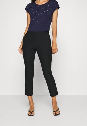 Woman wearing navy blue short-sleeve top with small embellishments and black cropped straight-leg pants with black open-toe heels.
