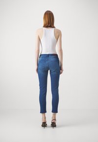 Fehér ujjatlan felső, kék pamut skinny farmernadrág, közepes derekú, öt zsebes kialakítással és egy kis barna bőr folttal a hátsó részen.