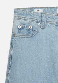 Lys blå denim-bukser med baggy design, frontlomme med sølvfarget metall, og kontrastsydd søm. Merket har teksten "BAGGY ALEX."