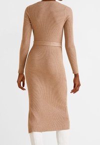 Robe en maille à manches longues de couleur beige clair avec une texture côtelée, une silhouette ajustée et une taille ceinturée, atteignant la longueur mi-mollet.
