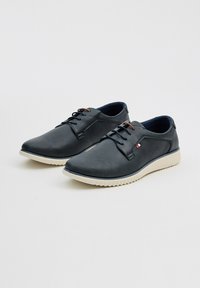 Zapatos de color azul marino oscuro con un acabado texturizado, diseño de cordones, suela de goma de color claro y pequeño detalle en rojo y blanco.