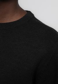 Zwart gebreid sweater met een ronde hals, die een zachte textuur en een gladde afwerking toont. Close-up weergave concentreert zich op de halslijn en het detail van de mouw.