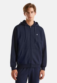 Námořnická mikina na zip z měkkého materiálu s přední kapsou, nastavitelnou kapucí se šňůrkou a logem na hrudi. Volný střih s žebrovanými manžetami.