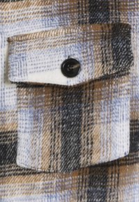 Flannelskjortestof med brunt, blåt og sort ternet mønster; har en brystlomme med hvide knapper og blød tekstur.