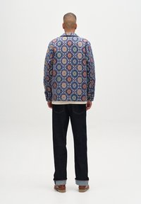 Jacke mit Floral-Muster in Blau-, Orange- und Grüntönen. Kombiniert mit dunklen Jeans und braunen Stiefeln, die einen lässigen Schnitt präsentieren.