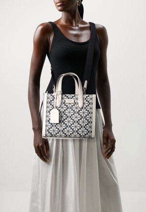 Weißes und marineblaues Handtasche mit floralem Muster, strukturiertem Design, doppelten Griffen, abnehmbaren Schultergurt und Etikett. Stoff mit glatter Textur.