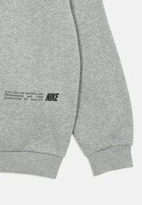 Manga de um moletom cinza e a bainha inferior mostrando o texto preto da Nike: "Nike e o Swoosh são marcas registradas e a sua garantia de qualidade."