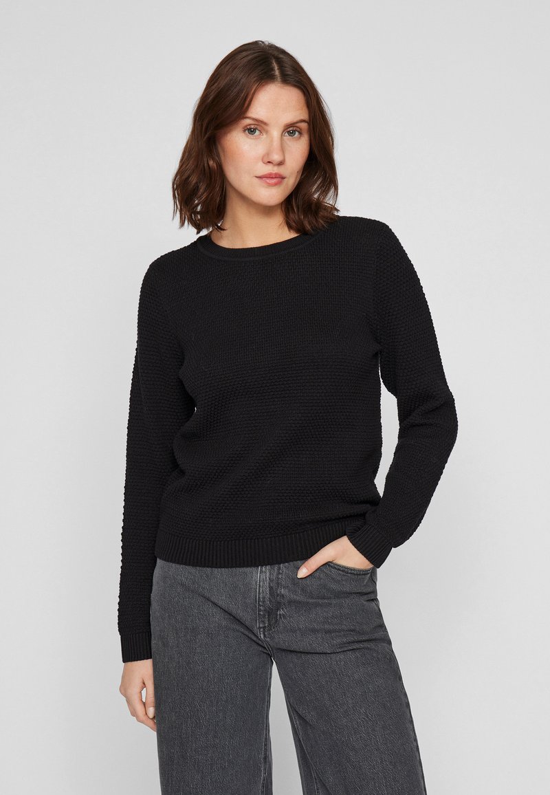 Μαύρο πλεκτό πουλόβερ με υφασ�μάτινο σχέδιο και ριμπ μανσέτες. Στρογγυλή λαιμόκοψη και μακριά μανίκια. Συνδυάζεται με γκρι τζιν.