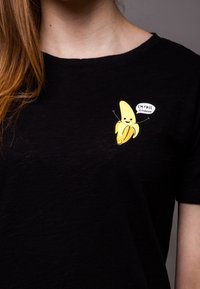 Black t-shirt with a yellow banana graphic on the left chest, featuring the text "I'M FREE Jihaaaa." Short sleeves and a relaxed fit.
