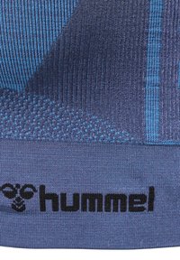 Blå idrottströja med texturerade vertikala ränder, en svart logotyp och ett kontrasterande blått mönster vid fållen.