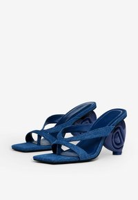 Blaue Jeans-Slingback-Absätze mit überkreuzten Riemen, quadratischen Zehen und einem markanten, geschwungenen dunkelblauen Absatz mit geprägtem Design.