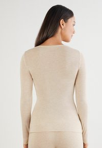 Beige Langarmoberteil aus weichem Stoff mit rundem Halsausschnitt und taillierter Silhouette. Die Nahtdetails sorgen für einen glatten Look.