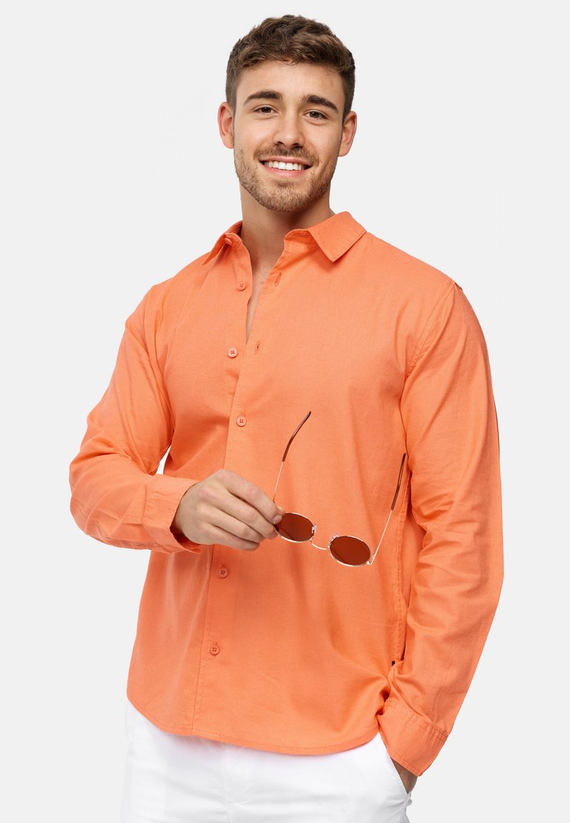Orange langærmet skjorte med knaplukning lavet af let stof, med en klassisk krave og iført aviator solbriller.