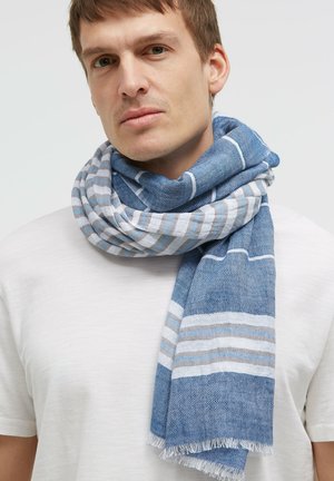 Man wearing white shirt and blue striped scarf wrapped around neck against gray background.