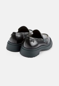 Černé lakované kožené slip-on boty s hladkým povrchem, zaobleným designem, silnou tmavou podrážkou a minimálními dekorativními akcenty.