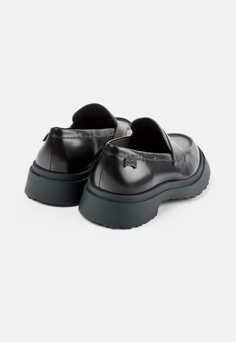 Chaussures noires en cuir verni à enfiler avec une finition lisse, un design arrondi, une semelle épaisse foncée et des accents décoratifs minimalistes.