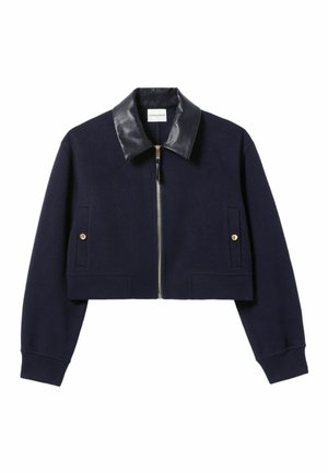 Veste cropped bleu marine avec un col en cuir noir, une fermeture éclair dorée et deux poches avant avec des boutons dorés. Tissu doux et poignets côtelés.