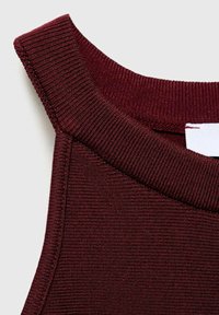 Gros plan sur un col de vêtement sans manches, côtelé, de couleur bordeaux foncé avec une étiquette blanche à l'intérieur.