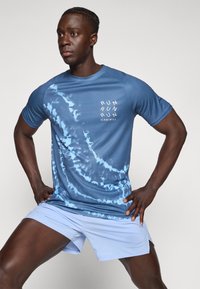 Blå tie-dye treningsskjorte med korte ermer som har hvit "RUN" tekst, og lyseblå shorts med mesh-struktur.