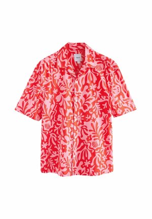 Homme marchant pieds nus sur une plage de sable, portant une chemise à manches courtes florale corail et rose vif et un short assorti.