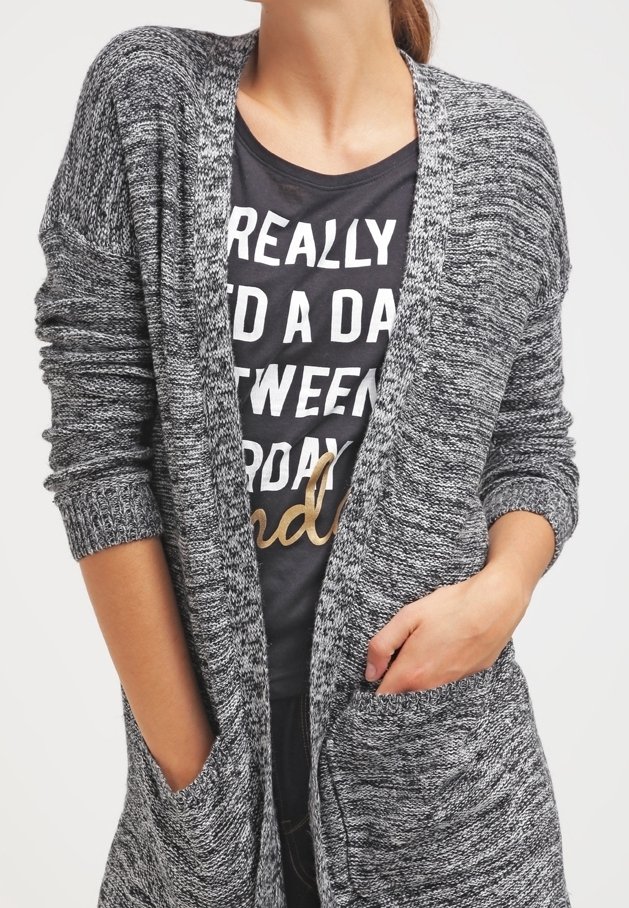 Szary dzianinowy kardigan o luźnym kroju, z długimi rękawami, otwartym przodem i dwoma przednimi kieszeniami, nałożony na czarny t-shirt z białym napisem.