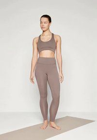Braháló sportmelltartó és illeszkedő, magas derekú leggings páros egy tompa barna árnyalatban. Az anyag simának tűnik, és testhezálló dizájnja aktív viseletre alkalmas.