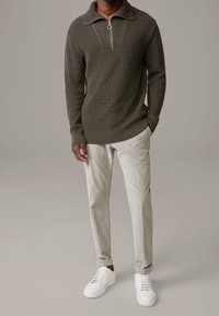 Pull-over en maille olive avec un col zippé et un motif texturé, associé à un pantalon en velours côtelé gris clair et des baskets blanches, affichant un look décontracté.