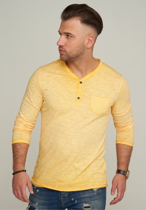 Yellow long-sleeve henley shirt with a textured pattern, three-button placket, and a chest pocket. Edges feature contrasting orange stitching.