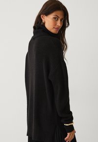 Sort strikket turtleneck sweater med en afslappet pasform, struktureret stof, nedsænkede skuldre og slidsse ved kanten.