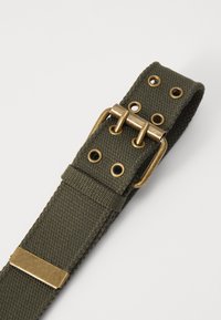 Olive green canvas strap with brass hardware, featuring metal grommets and a rectangular buckle for adjustment and fastening.