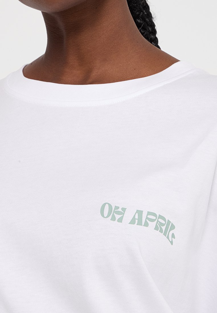 Weißes T-Shirt mit kurzen Ärmeln und rundem Ausschnitt, auf der linken Seite mit grünem Text "OH APRIL" in einem geschwungenen Design.