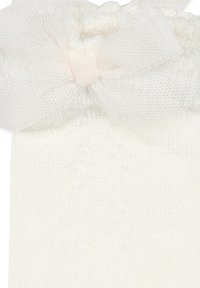 Calzino bianco di maglia con un morbido fiocco in tulle trasparente nella parte superiore. Caratterizzato da una texture liscia e un design semplice e classico.