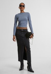 Ljusblå långärmad topp, figurnära. Höga svarta denimkjol med en slits framtill. Svarta klackstövlar och en glittrig svart handväska med kedja.