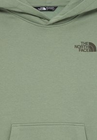 Casaco de moletão verde-claro feito de tecido suave, com um bolso na frente. Apresenta um pequeno logotipo escuro no peito e um capuz clássico com cordão.