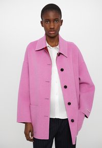 Pink wool coat with a collared neck, oversized fit, front button closure, two side pockets, and subtle stitching details.