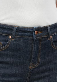 Mørkeblå denimjeans med kobberdetaljer. Egenskaper inkluderer et rett snitt, synlige sømmer og en frontknapplukking.